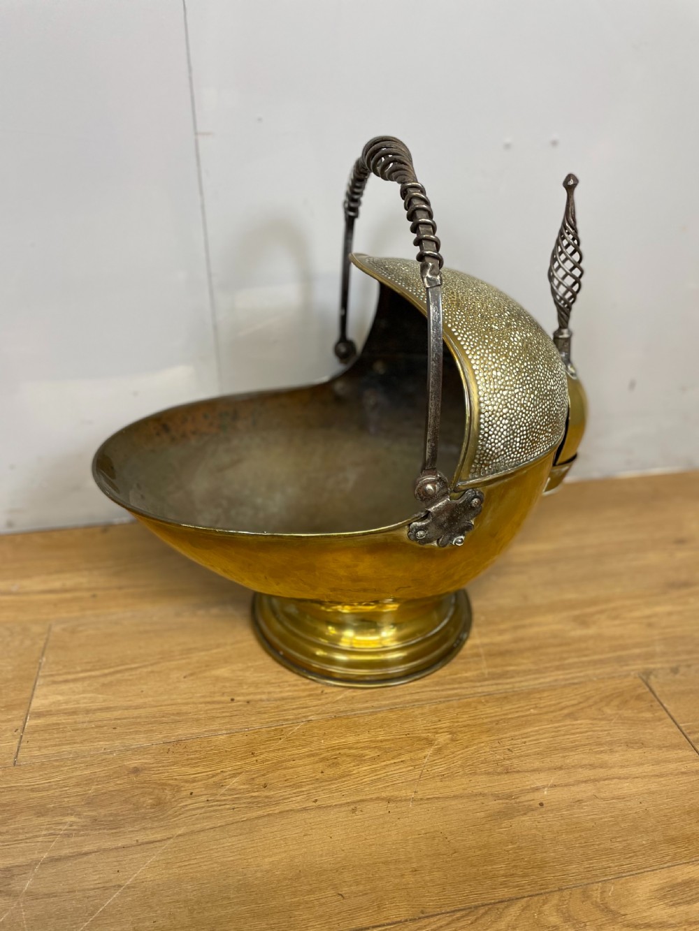 An Arts and Crafts style brass coal helmet with a textured hood, a wire-wrapped swing handle, a round pedestal base, and a matching hand shovel.