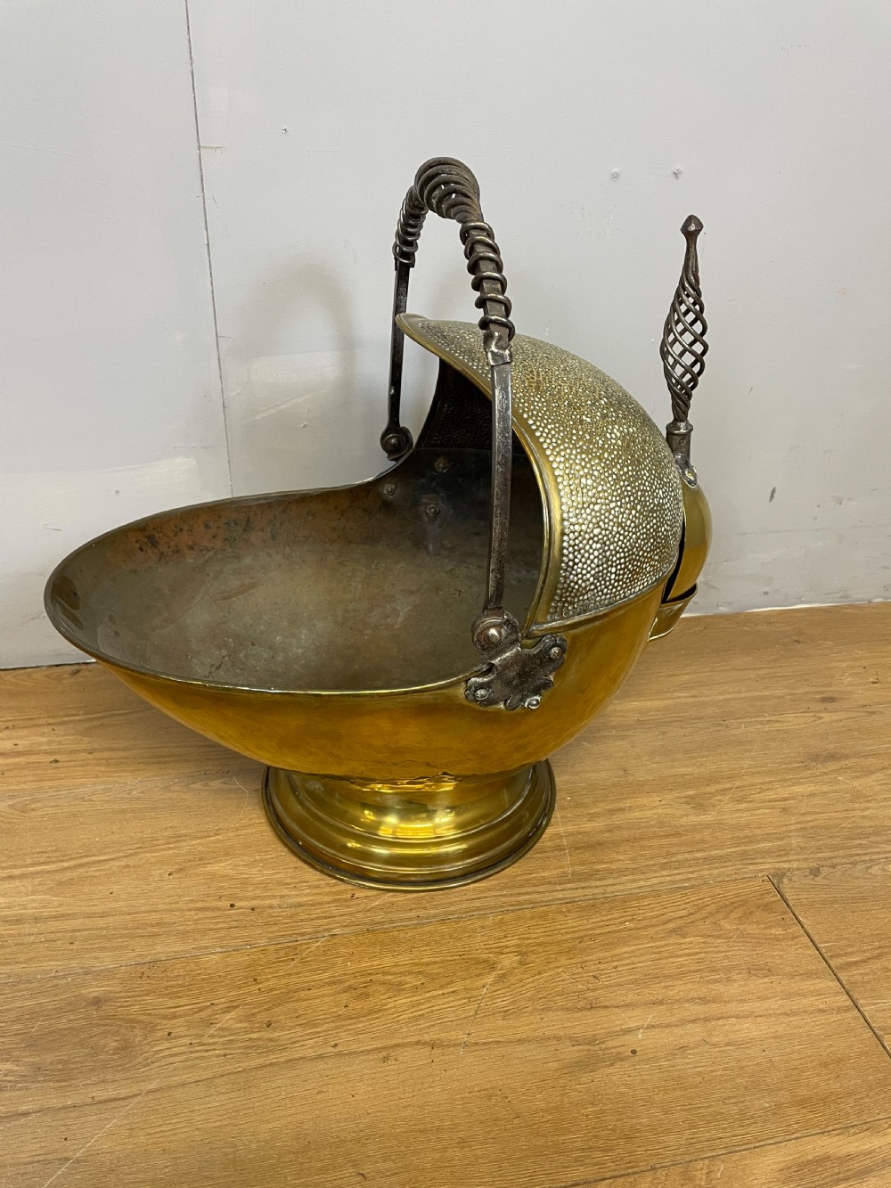 An Arts and Crafts style brass coal helmet with a textured hood, a wire-wrapped swing handle, a round pedestal base, and a matching hand shovel. View II
