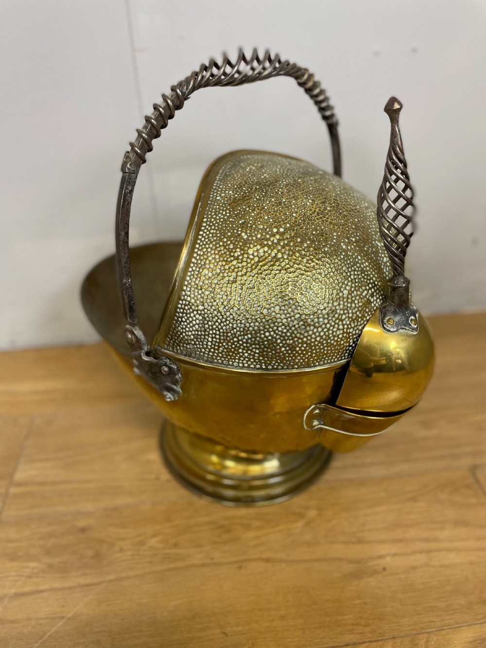 An Arts and Crafts style brass coal helmet with a textured hood, a wire-wrapped swing handle, a round pedestal base, and a matching hand shovel. View III
