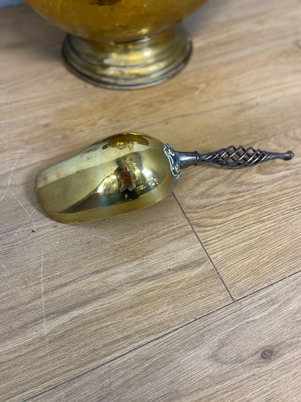 An Arts and Crafts style brass coal helmet with a textured hood, a wire-wrapped swing handle, a round pedestal base, and a matching hand shovel. View VI