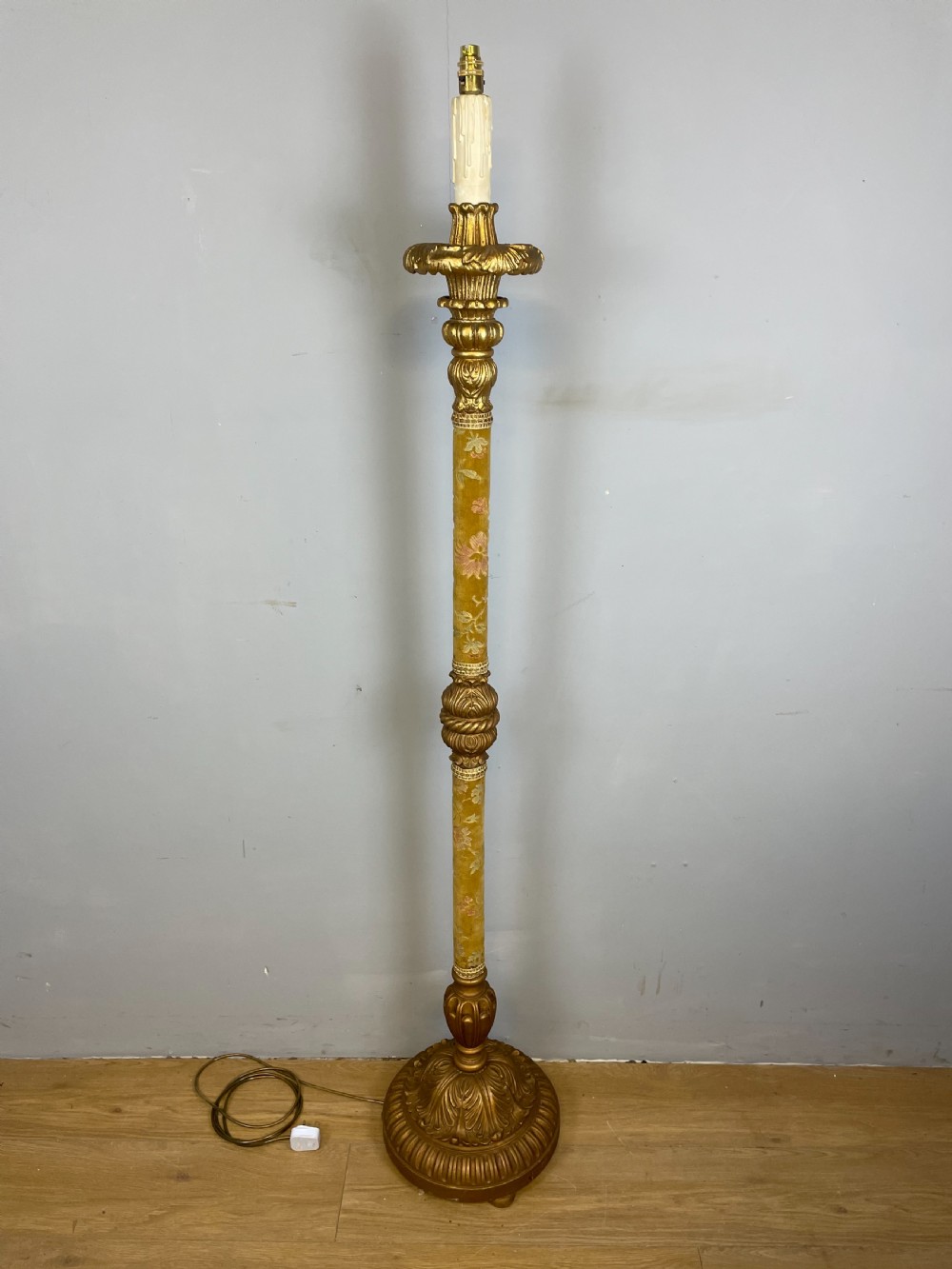 An Italian carved giltwood standard lamp with floral fabric central column details and a leaf-carved circular base.