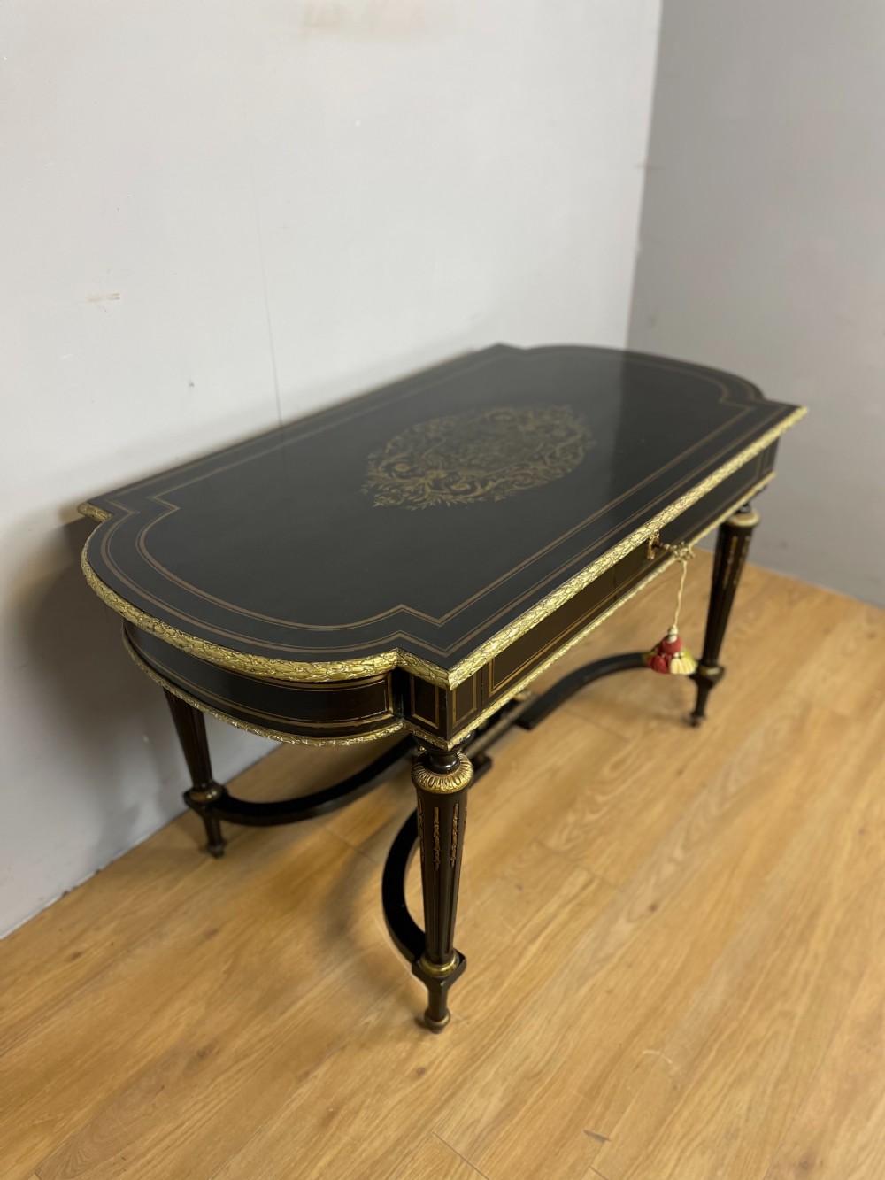 An ebonised nineteenth-century French writing table featuring gilt-bronze mounts, fluted tapered legs, a single central drawer, and a shaped top with central marquetry detailing. View IV
