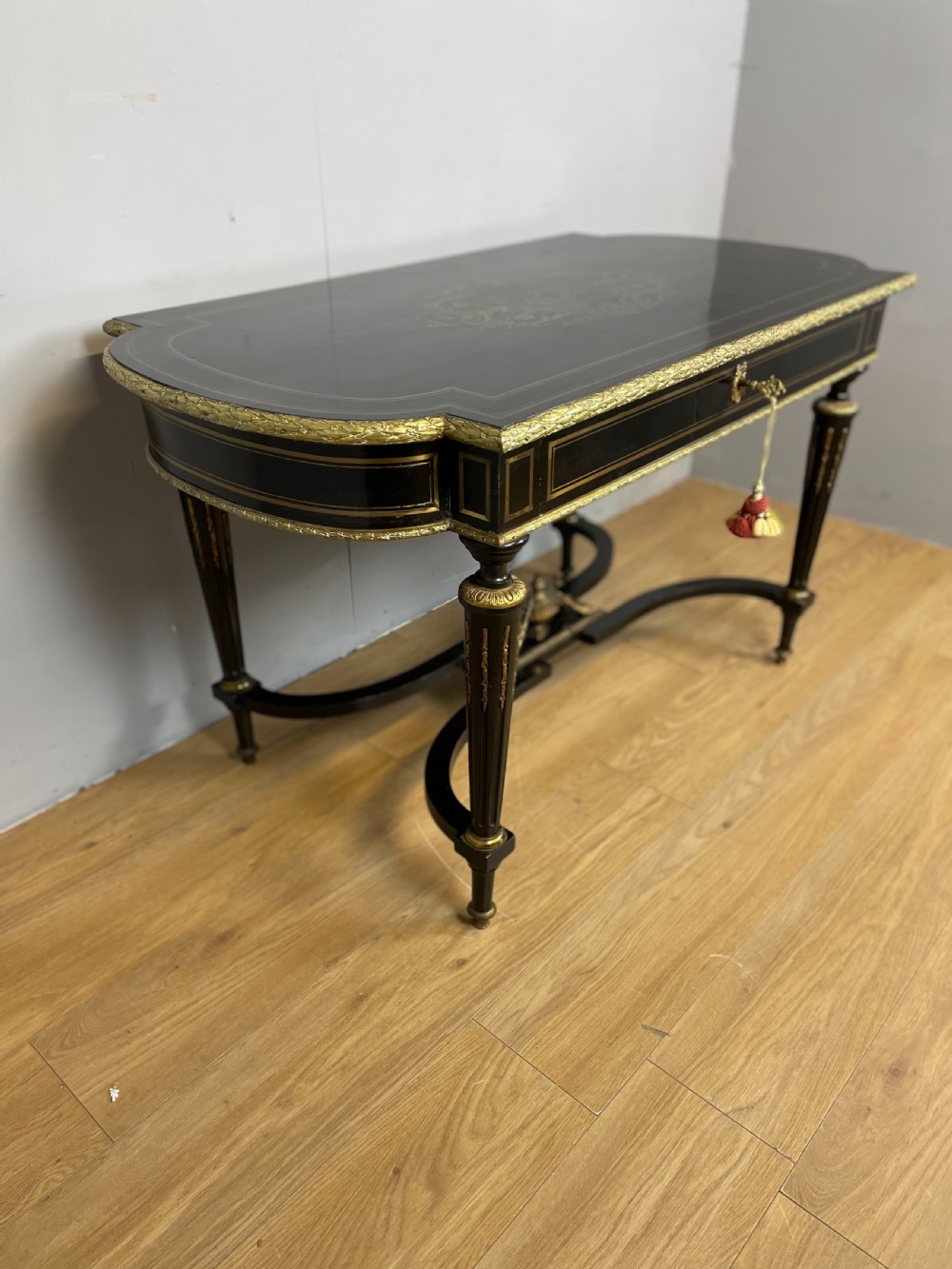 An ebonised nineteenth-century French writing table featuring gilt-bronze mounts, fluted tapered legs, a single central drawer, and a shaped top with central marquetry detailing. View VI