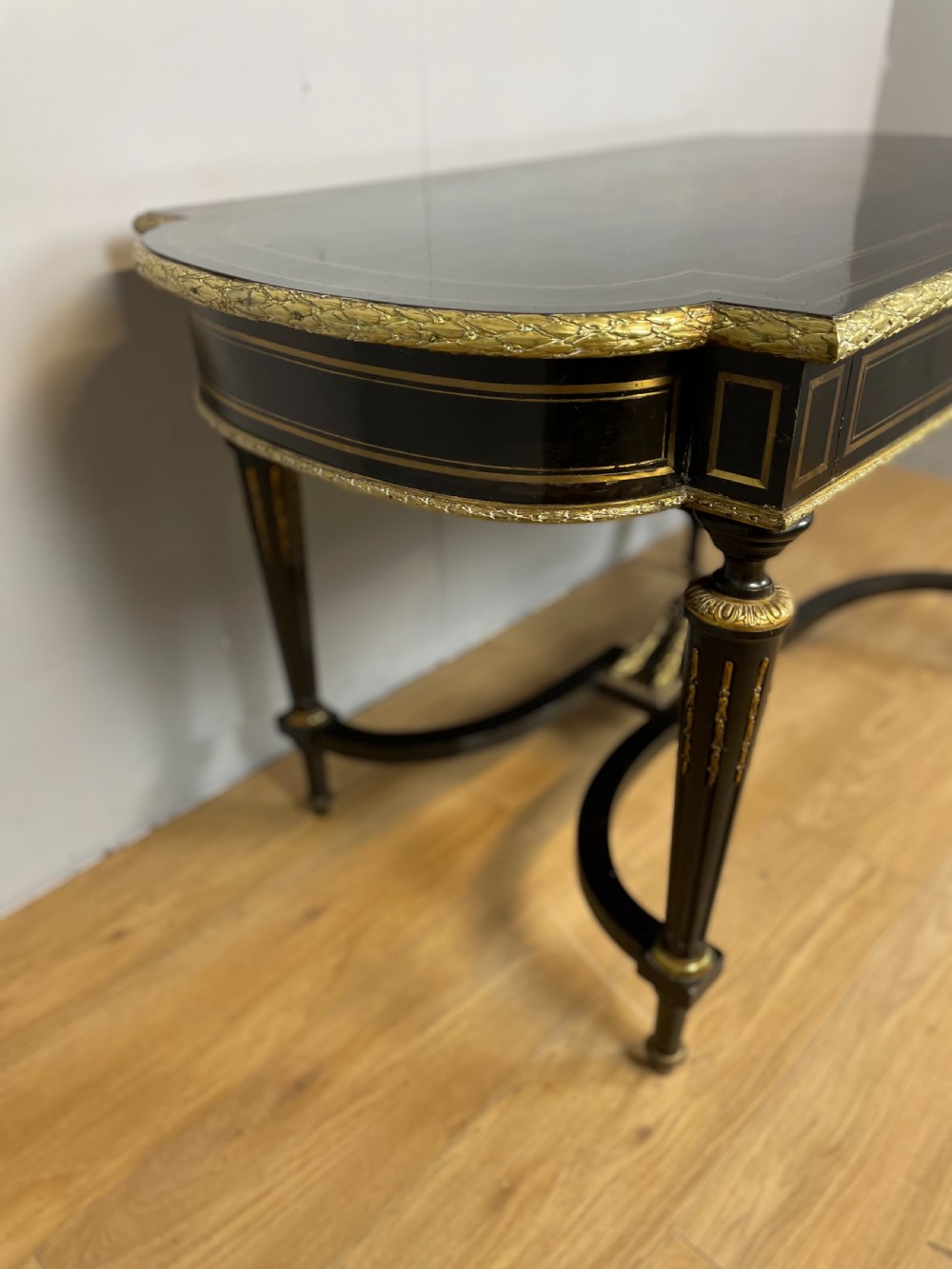 An ebonised nineteenth-century French writing table featuring gilt-bronze mounts, fluted tapered legs, a single central drawer, and a shaped top with central marquetry detailing. View VII
