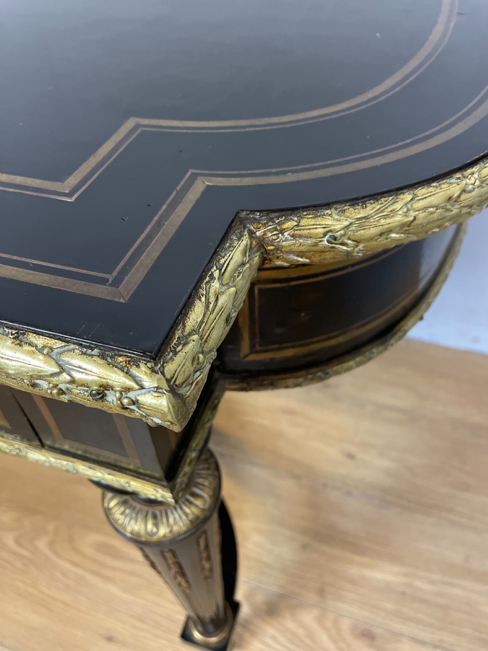 An ebonised nineteenth-century French writing table featuring gilt-bronze mounts, fluted tapered legs, a single central drawer, and a shaped top with central marquetry detailing. View X