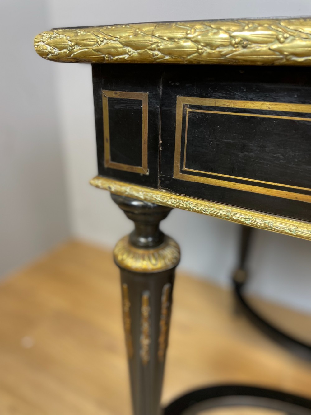 An ebonised nineteenth-century French writing table featuring gilt-bronze mounts, fluted tapered legs, a single central drawer, and a shaped top with central marquetry detailing. View XI