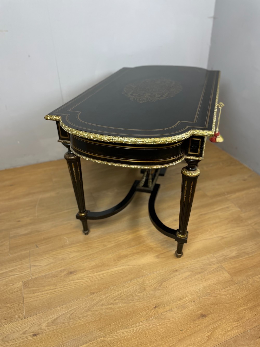 An ebonised nineteenth-century French writing table featuring gilt-bronze mounts, fluted tapered legs, a single central drawer, and a shaped top with central marquetry detailing. View XIII