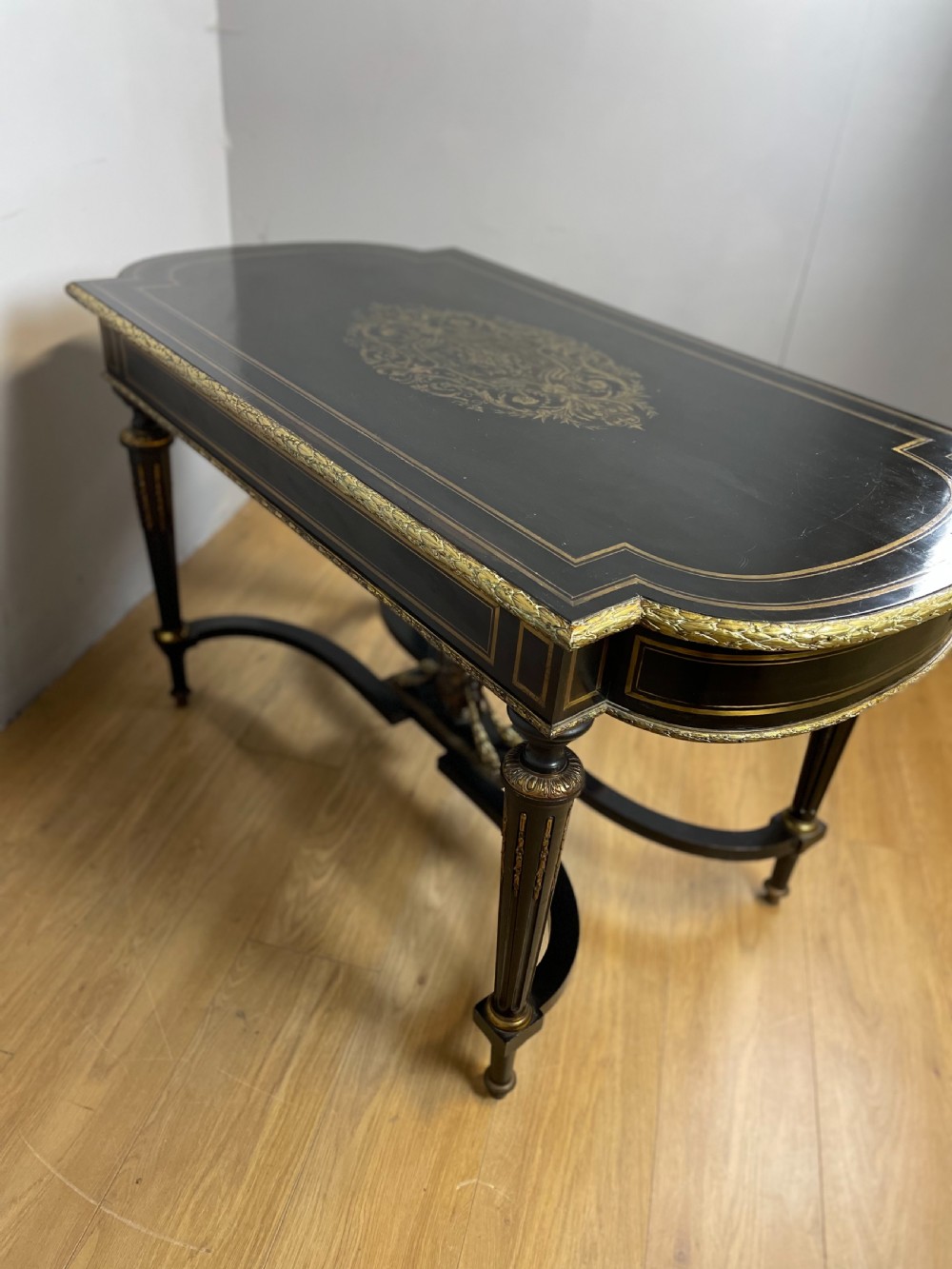 An ebonised nineteenth-century French writing table featuring gilt-bronze mounts, fluted tapered legs, a single central drawer, and a shaped top with central marquetry detailing. View XIV