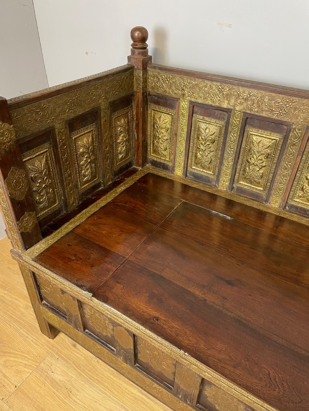 An Anglo Indian dark hardwood box settle featuring embossed brass panels, turned corner finials, and a hinged lift-top seat. View III