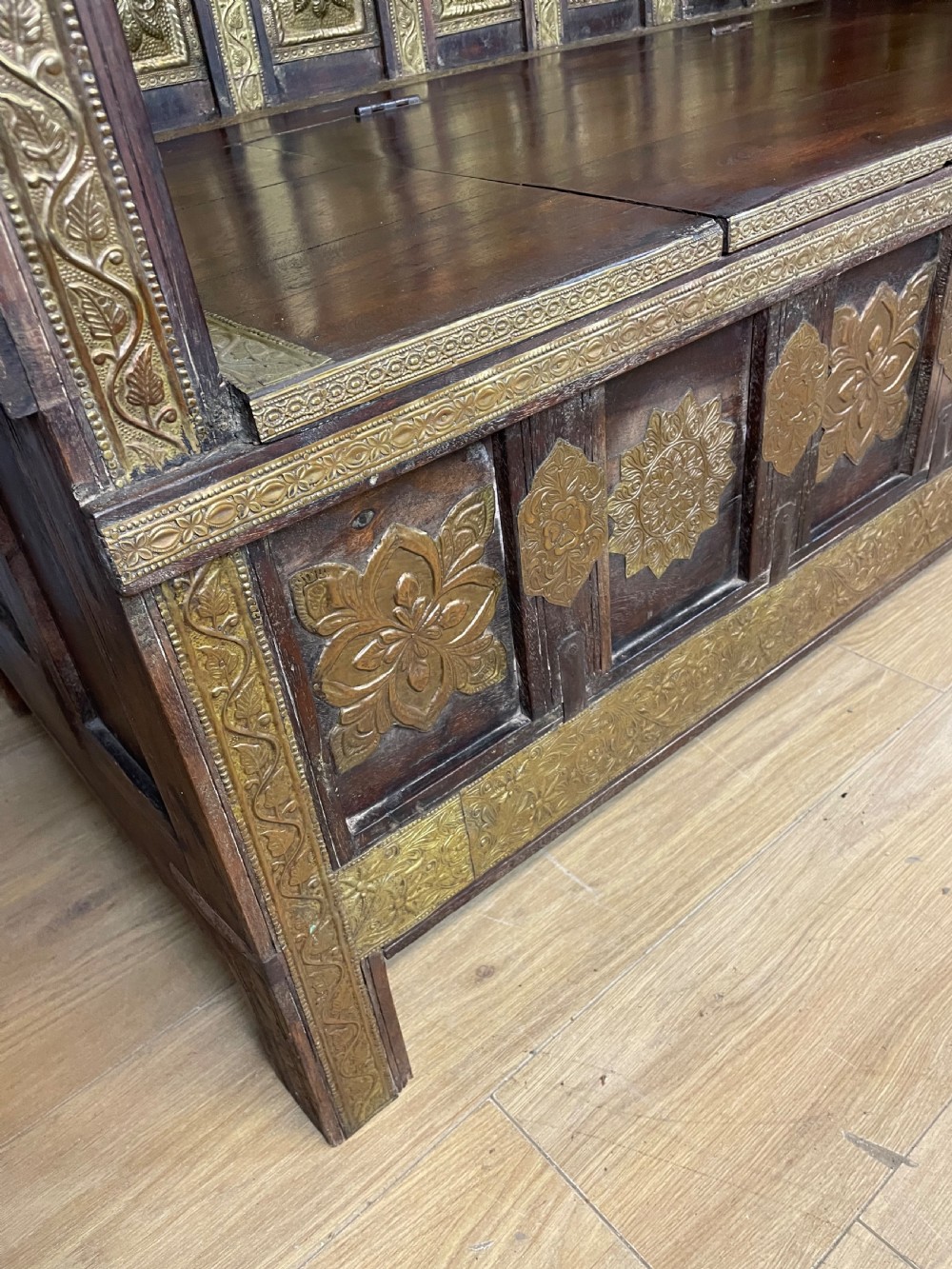 An Anglo Indian dark hardwood box settle featuring embossed brass panels, turned corner finials, and a hinged lift-top seat. View VII