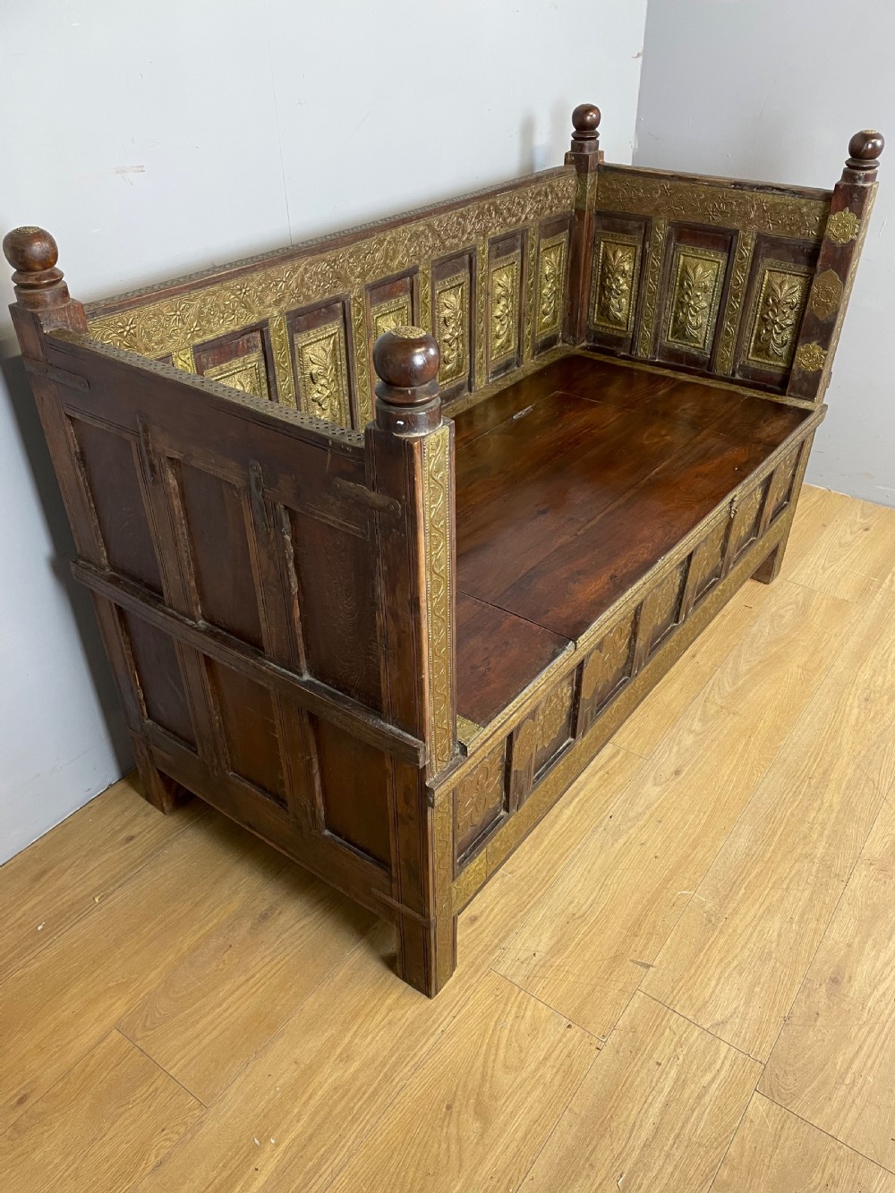 An Anglo Indian dark hardwood box settle featuring embossed brass panels, turned corner finials, and a hinged lift-top seat. View VIII