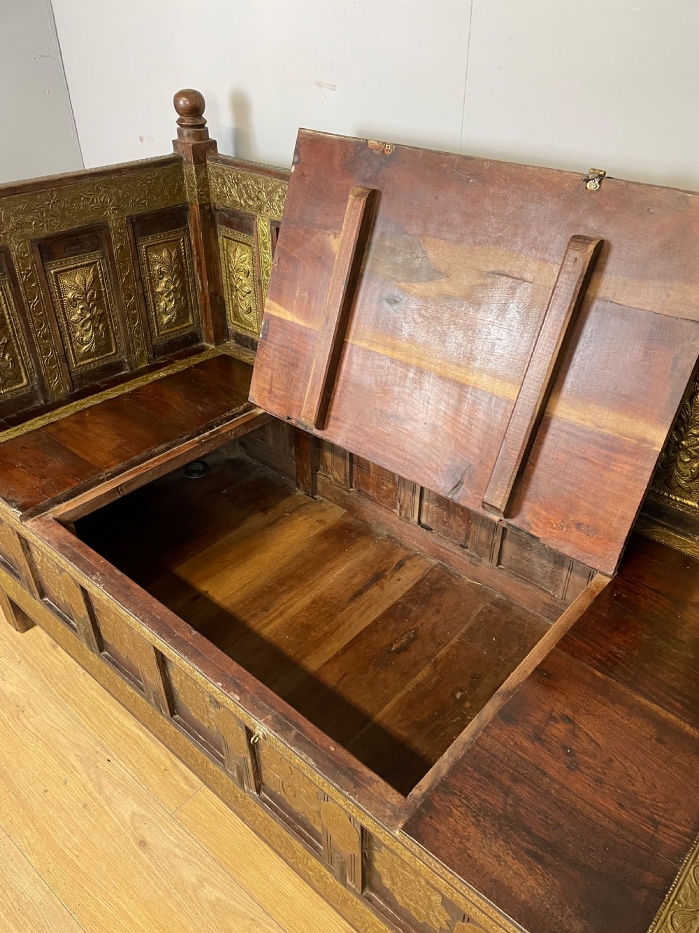 An Anglo Indian dark hardwood box settle featuring embossed brass panels, turned corner finials, and a hinged lift-top seat. View X