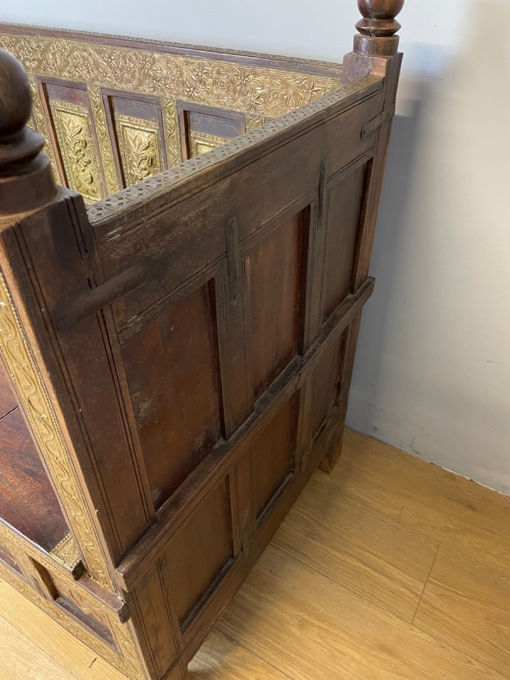 An Anglo Indian dark hardwood box settle featuring embossed brass panels, turned corner finials, and a hinged lift-top seat. View XII