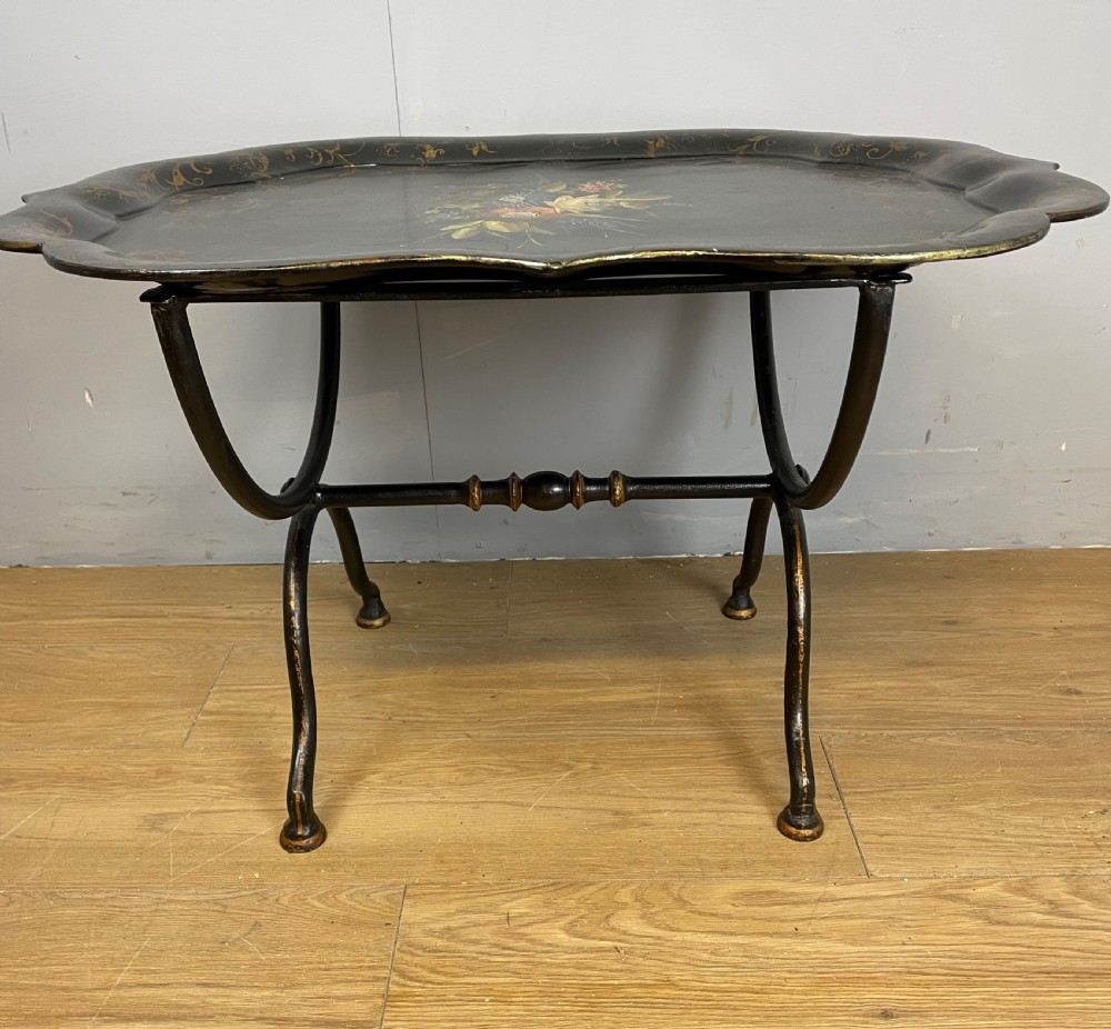 A nineteenth-century black lacquered papier-mache tray with scalloped edges and a central hand-painted floral motif resting on a black iron stand. View II