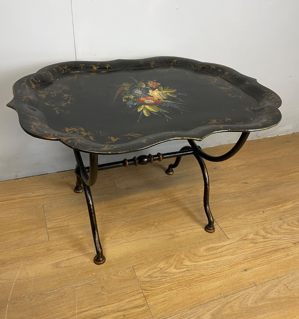A nineteenth-century black lacquered papier-mache tray with scalloped edges and a central hand-painted floral motif resting on a black iron stand. View III