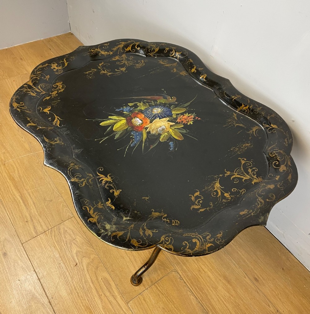 A nineteenth-century black lacquered papier-mache tray with scalloped edges and a central hand-painted floral motif resting on a black iron stand. View IV
