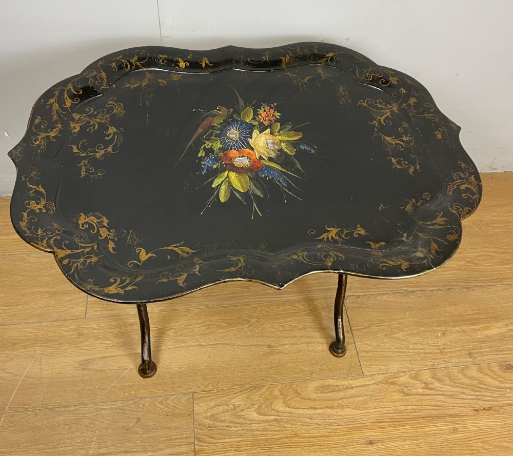 A nineteenth-century black lacquered papier-mache tray with scalloped edges and a central hand-painted floral motif resting on a black iron stand. View V