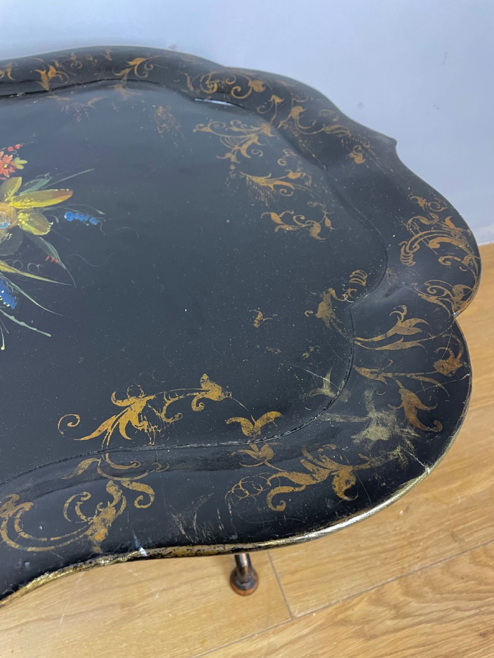 A nineteenth-century black lacquered papier-mache tray with scalloped edges and a central hand-painted floral motif resting on a black iron stand. View IX