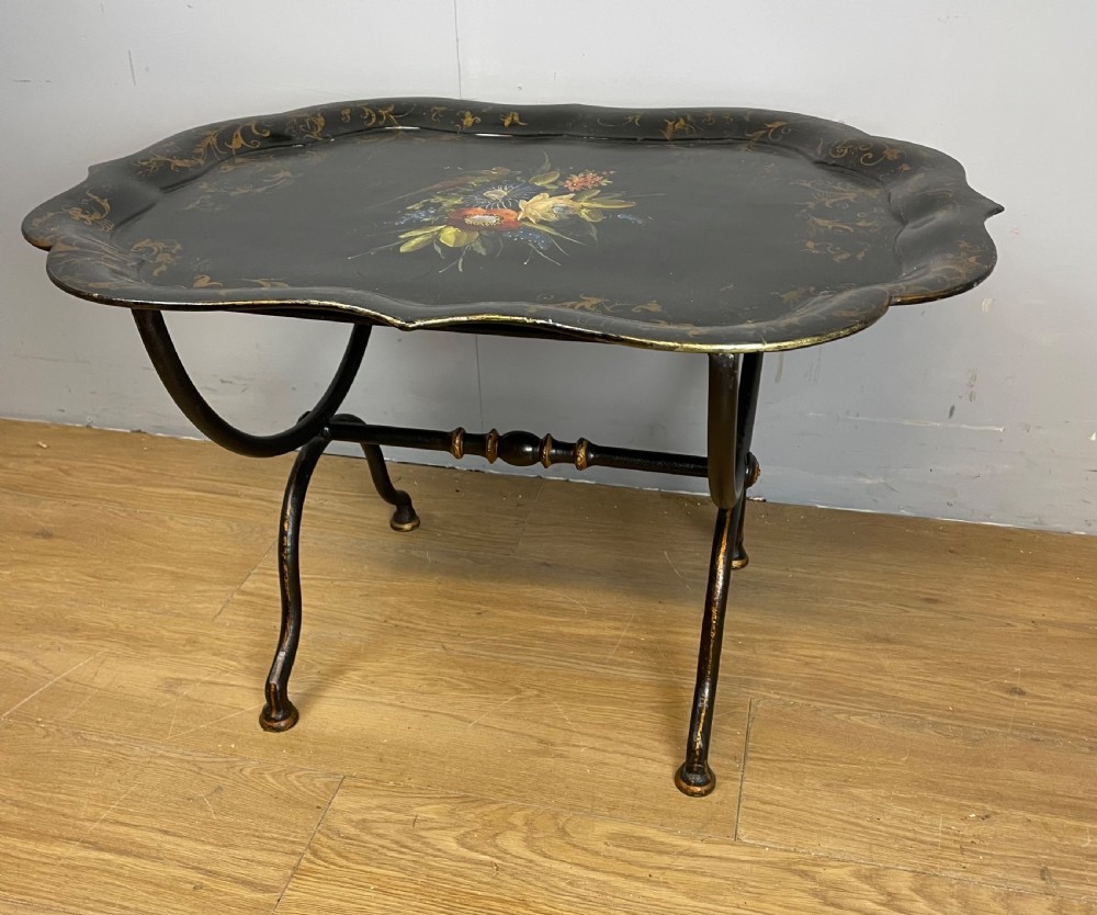 A nineteenth-century black lacquered papier-mache tray with scalloped edges and a central hand-painted floral motif resting on a black iron stand. View X