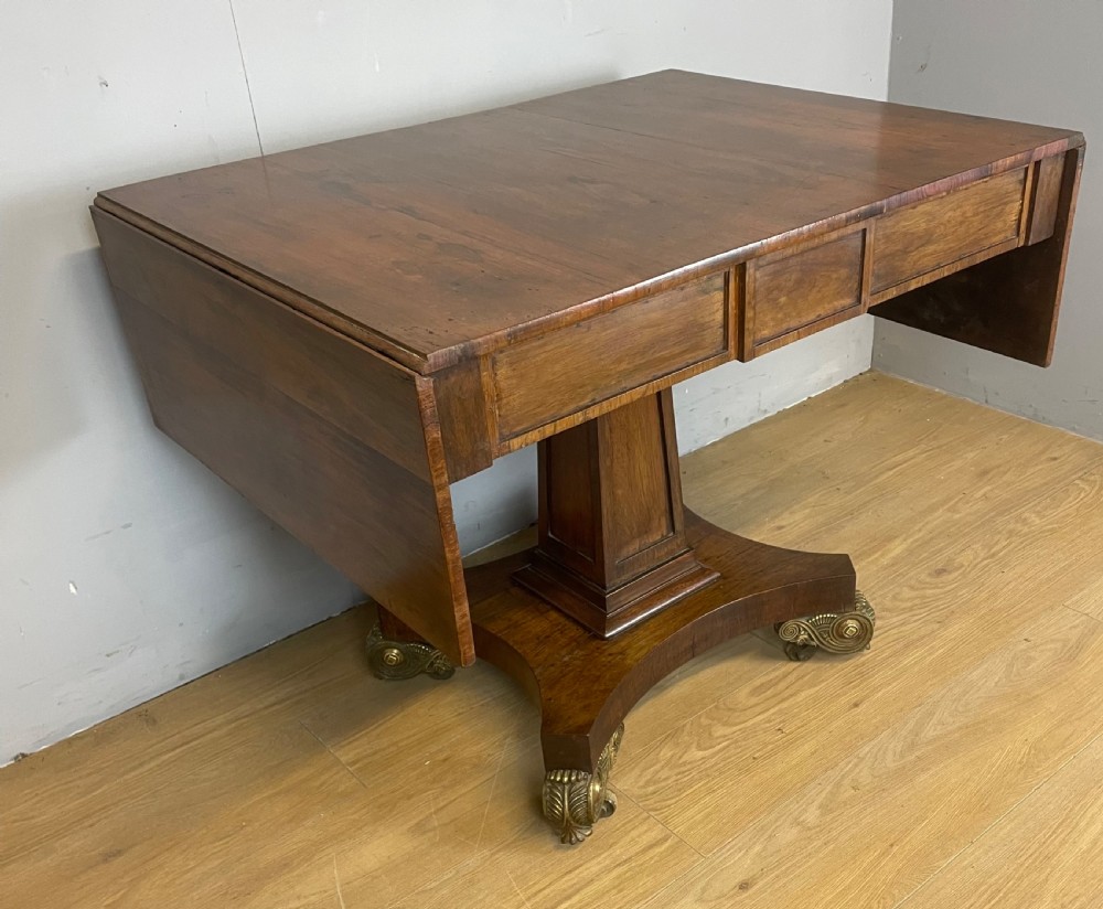 A Regency rosewood drop-leaf sofa table featuring two frieze drawers, a central column, and a quadruped platform base with decorative brass castors. View II