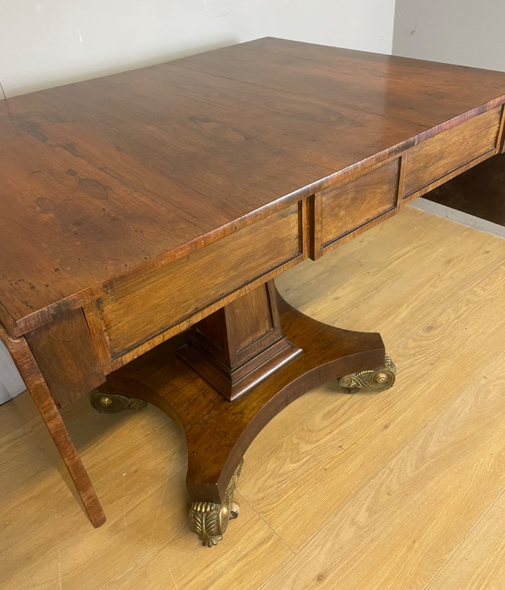 A Regency rosewood drop-leaf sofa table featuring two frieze drawers, a central column, and a quadruped platform base with decorative brass castors. View IV