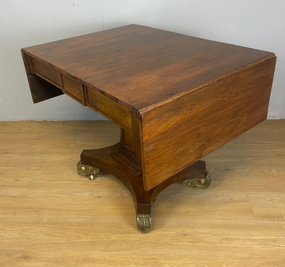 A Regency rosewood drop-leaf sofa table featuring two frieze drawers, a central column, and a quadruped platform base with decorative brass castors. View V