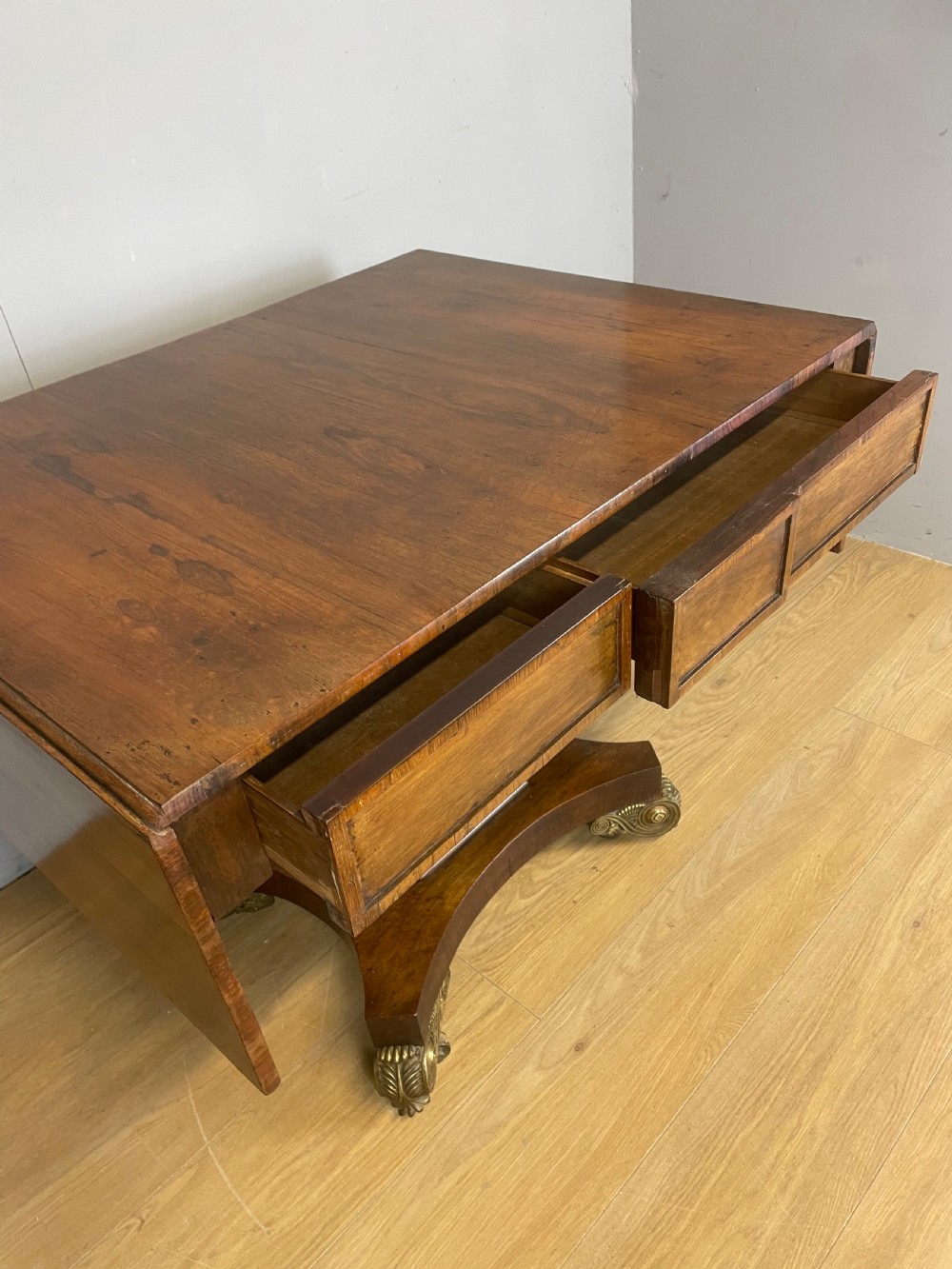 A Regency rosewood drop-leaf sofa table featuring two frieze drawers, a central column, and a quadruped platform base with decorative brass castors. View VII