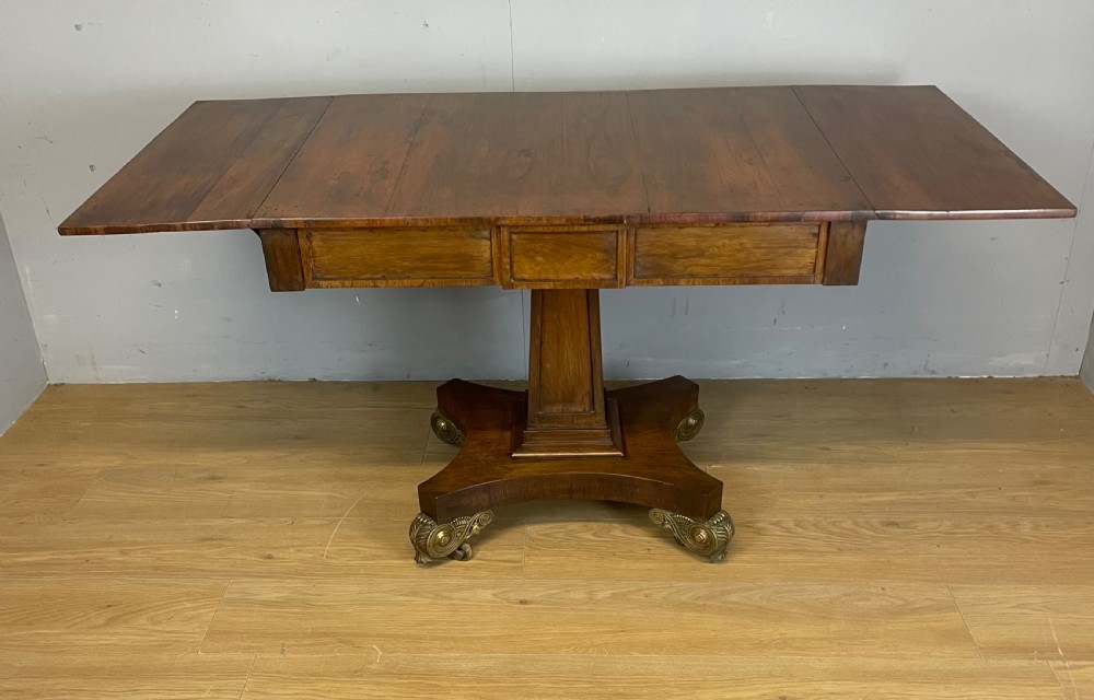 A Regency rosewood drop-leaf sofa table featuring two frieze drawers, a central column, and a quadruped platform base with decorative brass castors. View VIII