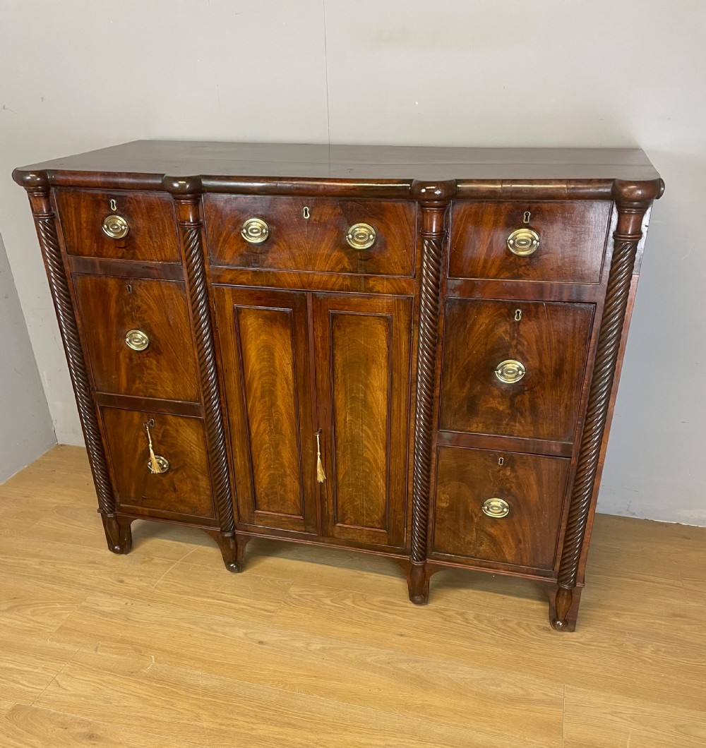 A Regency flame mahogany sideboard featuring rope-twist corner columns, multiple drawers with brass ring handles, and central cupboard doors.