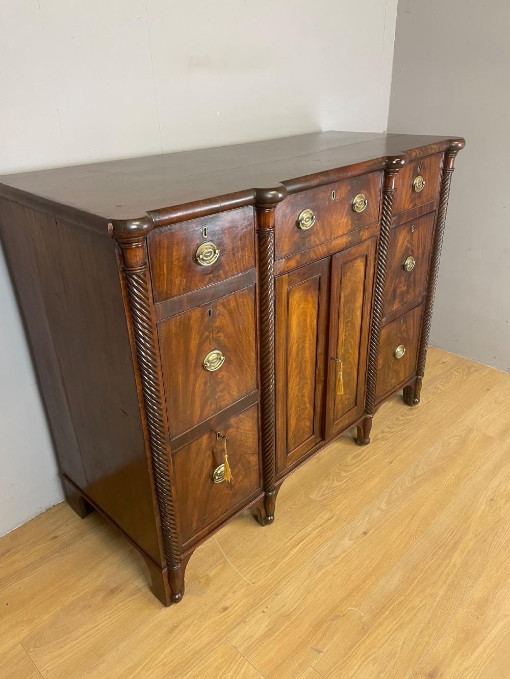 A Regency flame mahogany sideboard featuring rope-twist corner columns, multiple drawers with brass ring handles, and central cupboard doors. View II