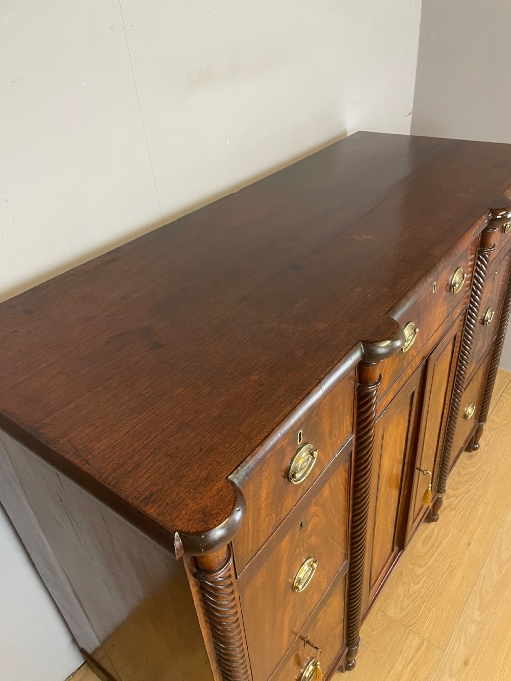 A Regency flame mahogany sideboard featuring rope-twist corner columns, multiple drawers with brass ring handles, and central cupboard doors. View V
