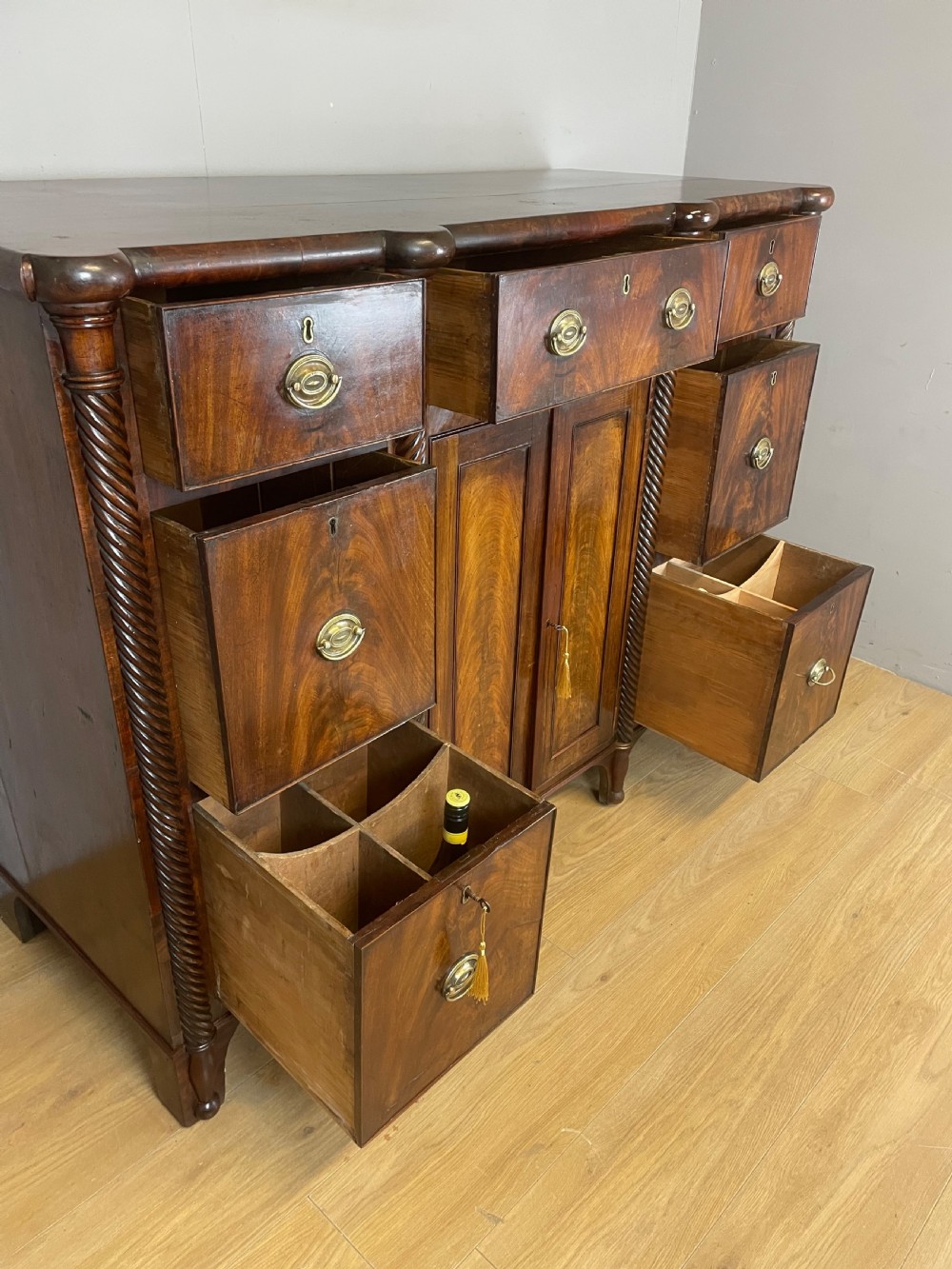A Regency flame mahogany sideboard featuring rope-twist corner columns, multiple drawers with brass ring handles, and central cupboard doors. View VII