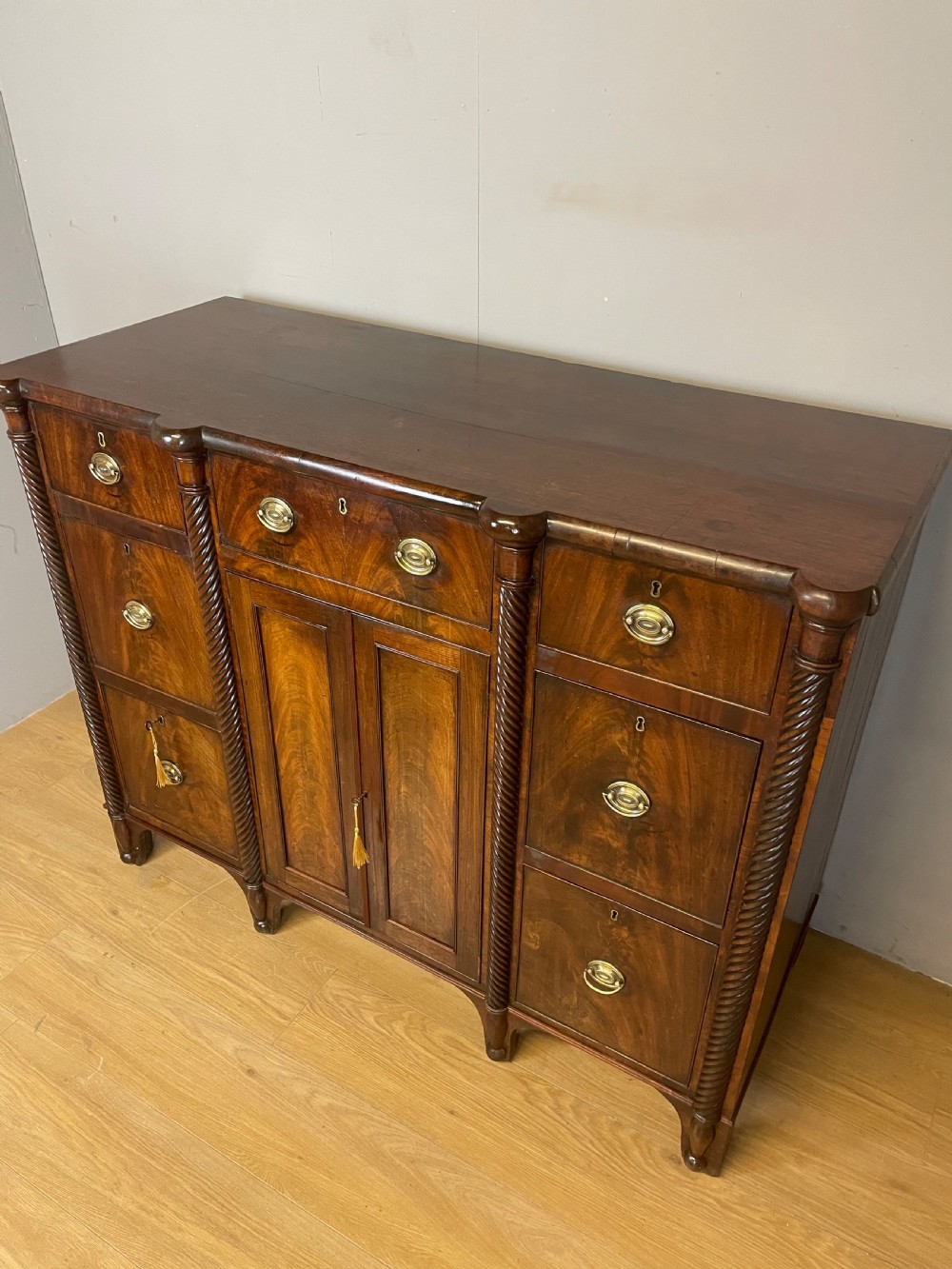 A Regency flame mahogany sideboard featuring rope-twist corner columns, multiple drawers with brass ring handles, and central cupboard doors. View XI
