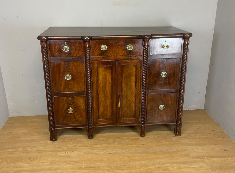 A Regency flame mahogany sideboard featuring rope-twist corner columns, multiple drawers with brass ring handles, and central cupboard doors. View XIV