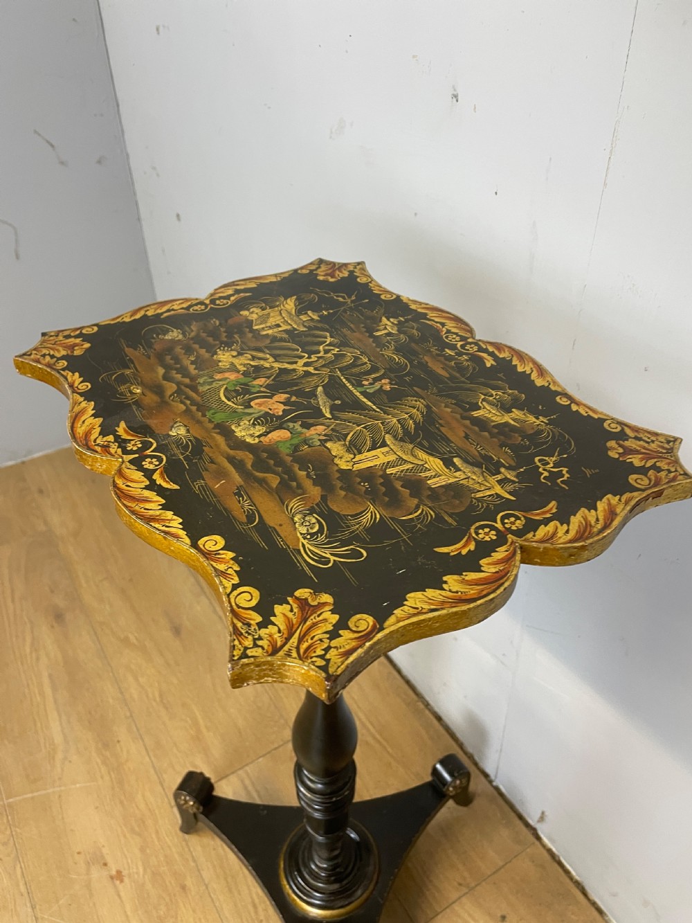 A nineteenth-century Chinoiserie wine table featuring a scalloped black lacquered top with gilded oriental landscape decoration, supported by a turned ebonised column on a tripartite base. View VI