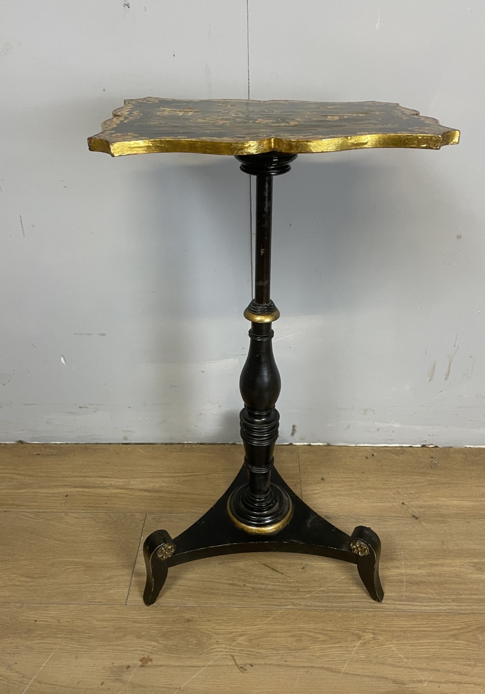 A nineteenth-century Chinoiserie wine table featuring a scalloped black lacquered top with gilded oriental landscape decoration, supported by a turned ebonised column on a tripartite base. View VIII