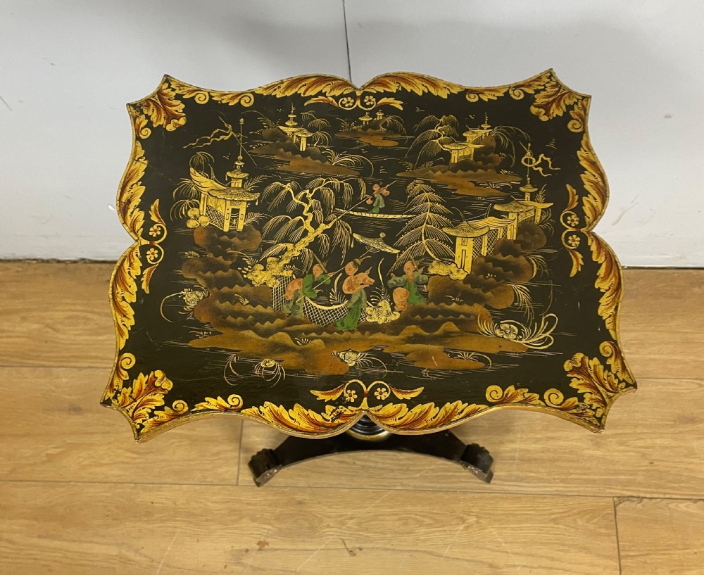A nineteenth-century Chinoiserie wine table featuring a scalloped black lacquered top with gilded oriental landscape decoration, supported by a turned ebonised column on a tripartite base. View IX