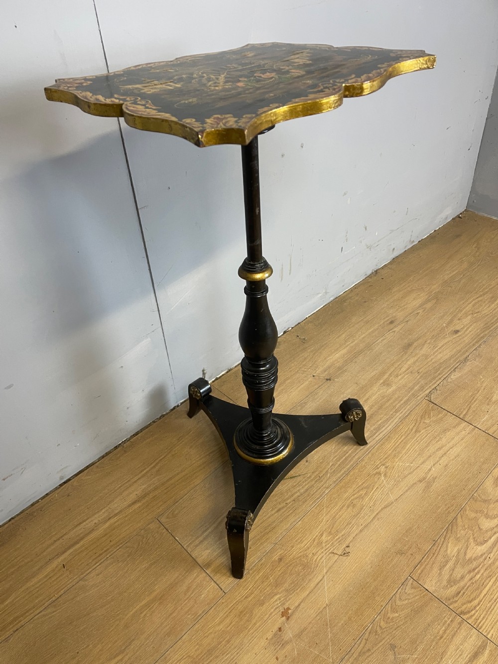 A nineteenth-century Chinoiserie wine table featuring a scalloped black lacquered top with gilded oriental landscape decoration, supported by a turned ebonised column on a tripartite base. View XI