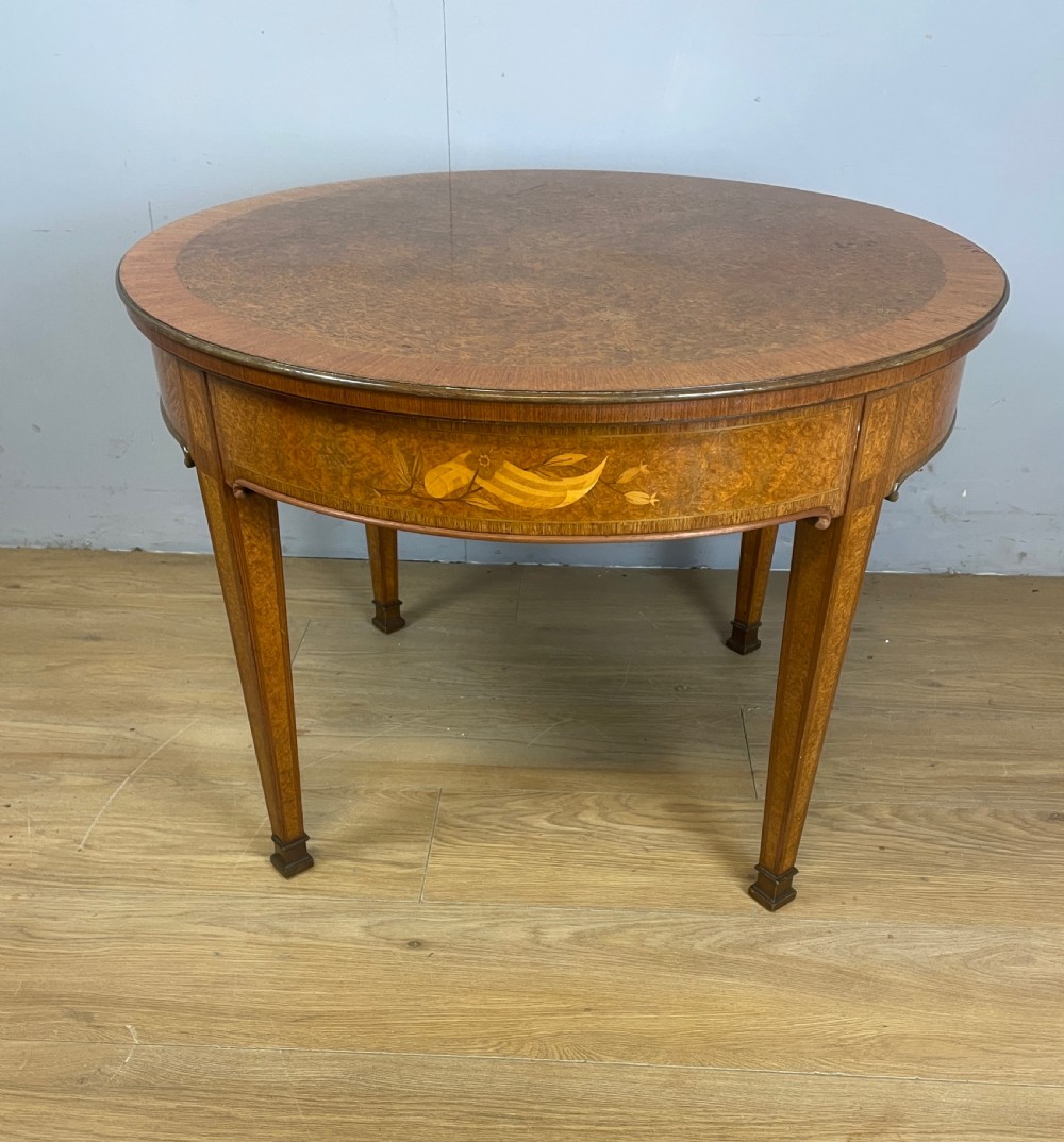 A circular 1930s burr walnut coffee table featuring floral marquetry on the apron and square tapered legs.