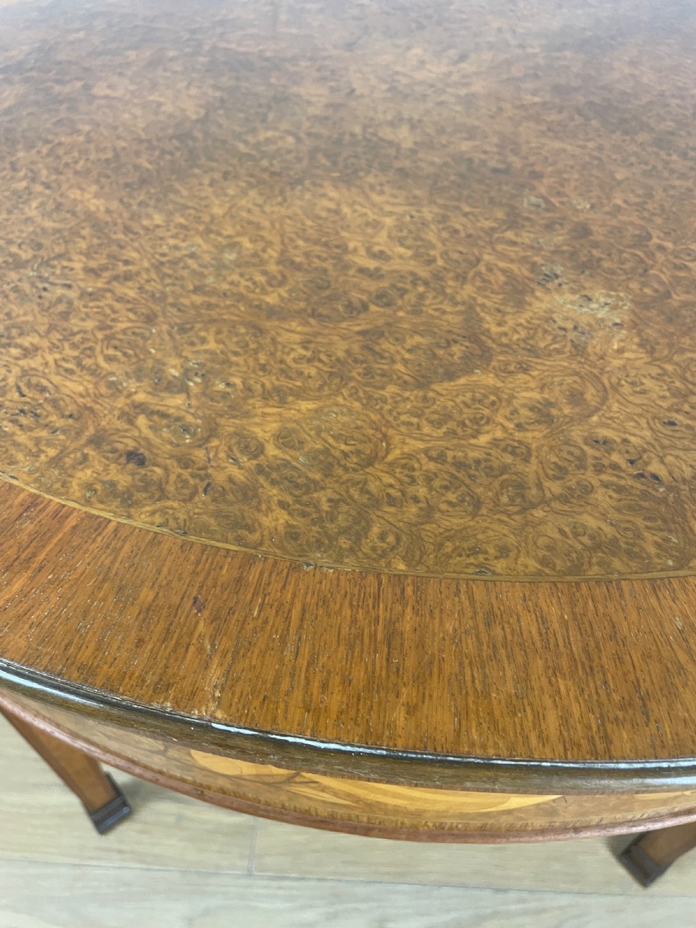 A circular 1930s burr walnut coffee table featuring floral marquetry on the apron and square tapered legs. View II