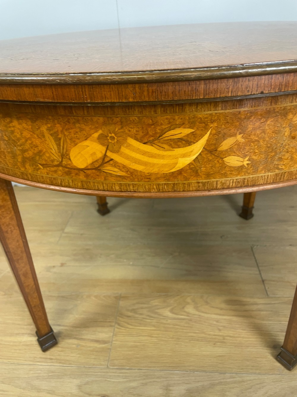A circular 1930s burr walnut coffee table featuring floral marquetry on the apron and square tapered legs. View IV