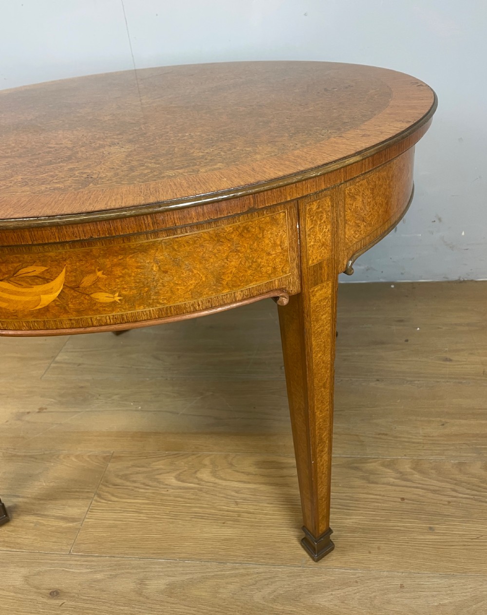 A circular 1930s burr walnut coffee table featuring floral marquetry on the apron and square tapered legs. View VI