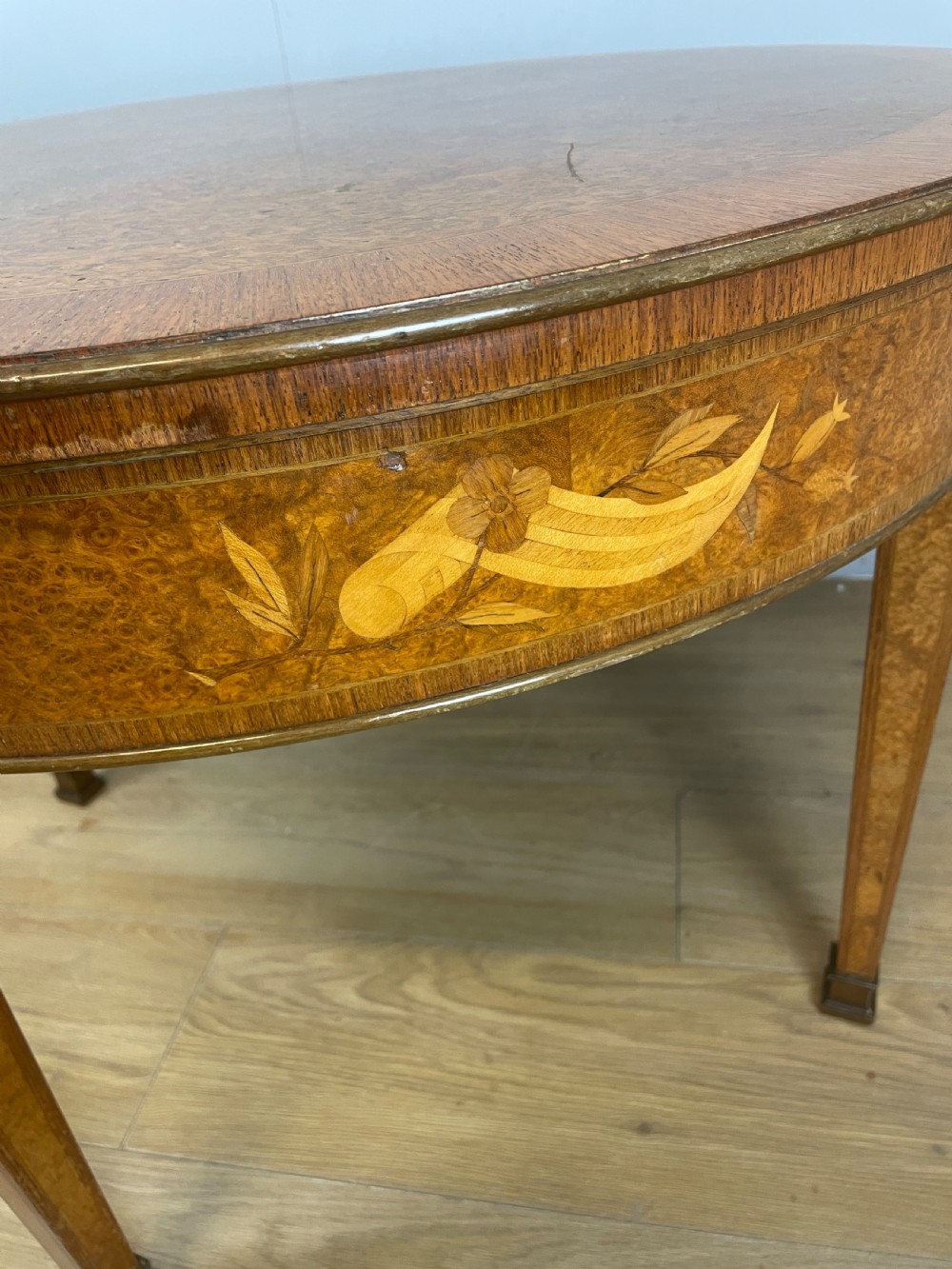 A circular 1930s burr walnut coffee table featuring floral marquetry on the apron and square tapered legs. View IX