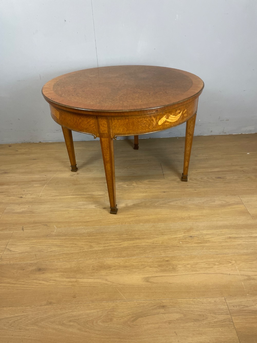 A circular 1930s burr walnut coffee table featuring floral marquetry on the apron and square tapered legs. View X