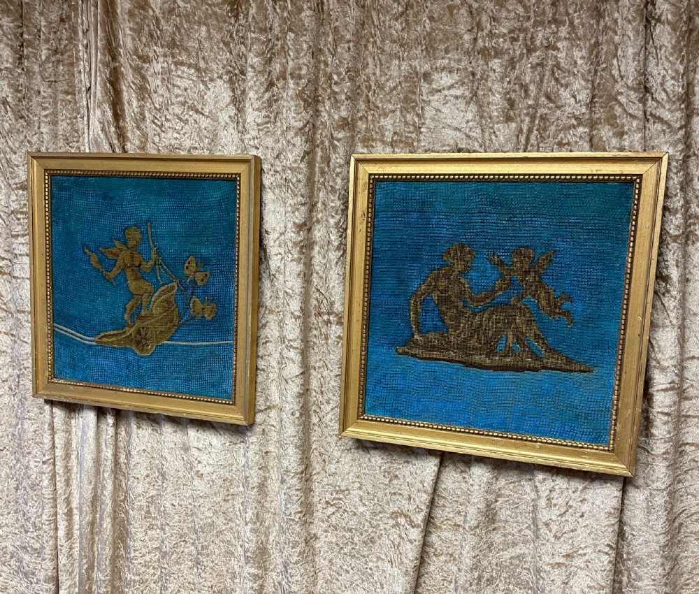 A pair of gilt-framed 19th-century needlework pictures featuring classical figures stitched in gold thread against a blue backdrop.