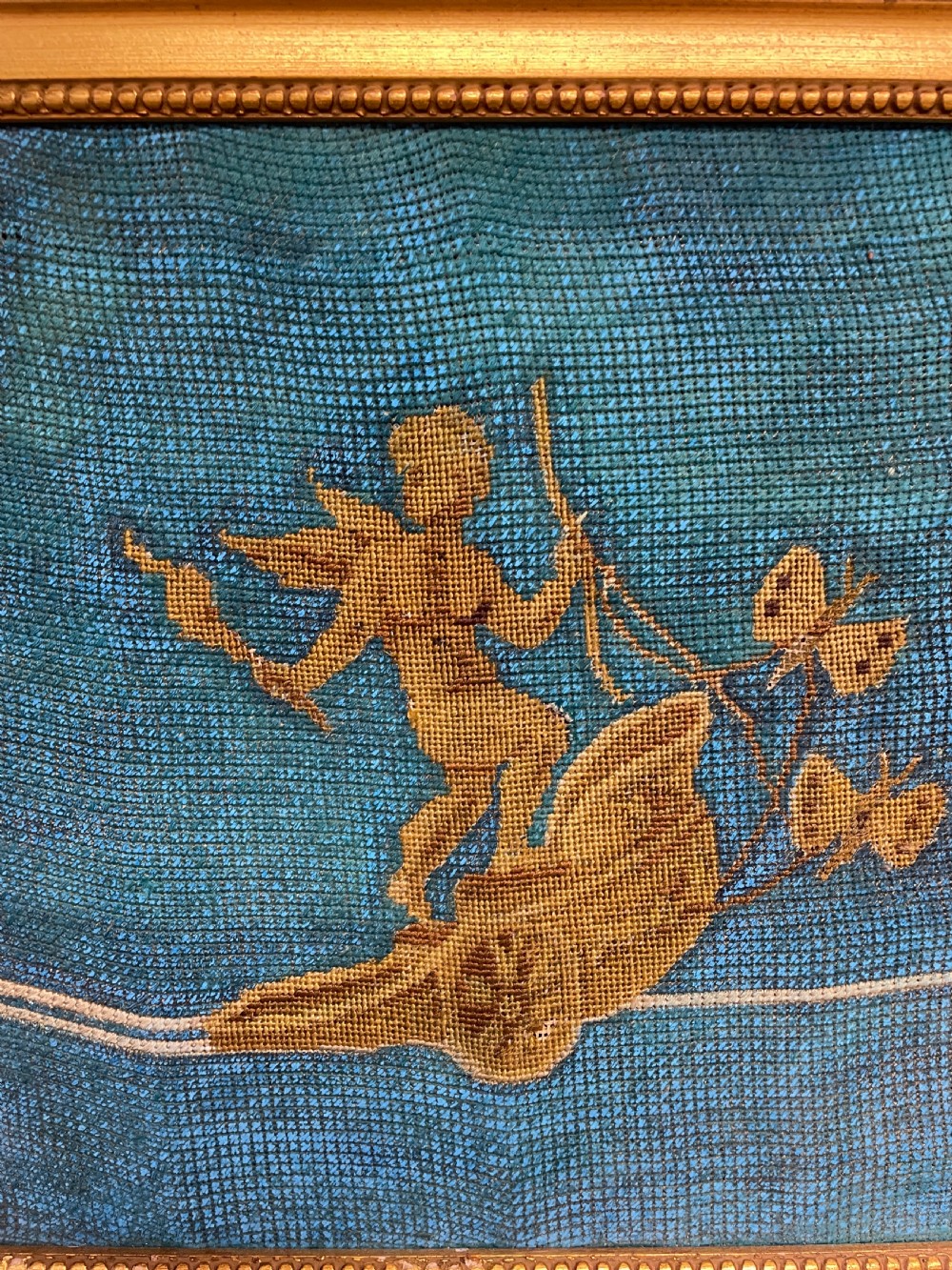A pair of gilt-framed 19th-century needlework pictures featuring classical figures stitched in gold thread against a blue backdrop. View V