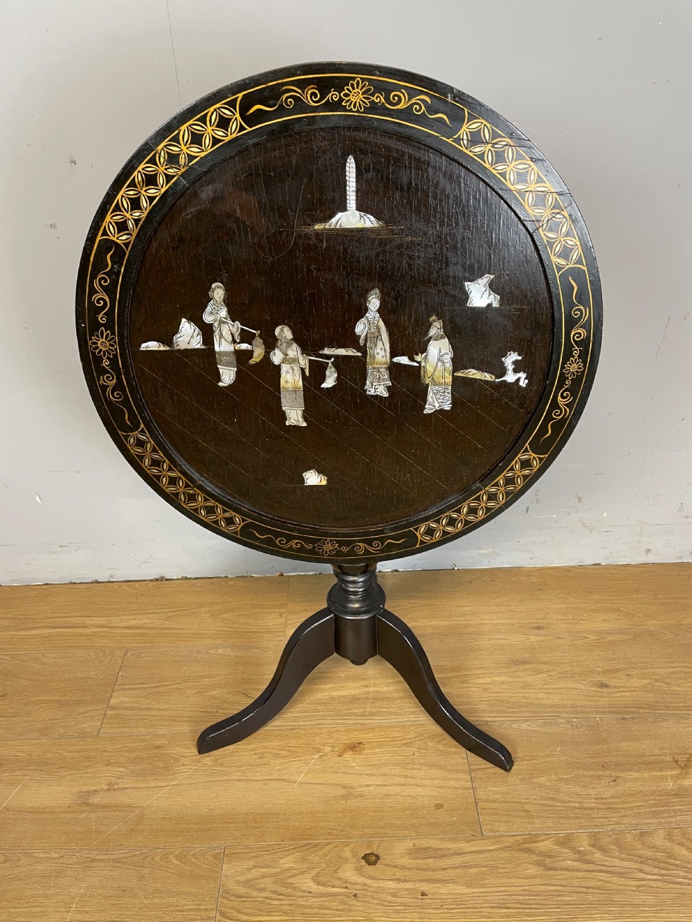 An Edwardian black lacquered circular tripod table decorated with mother-of-pearl figurative inlays and gilt floral borders.