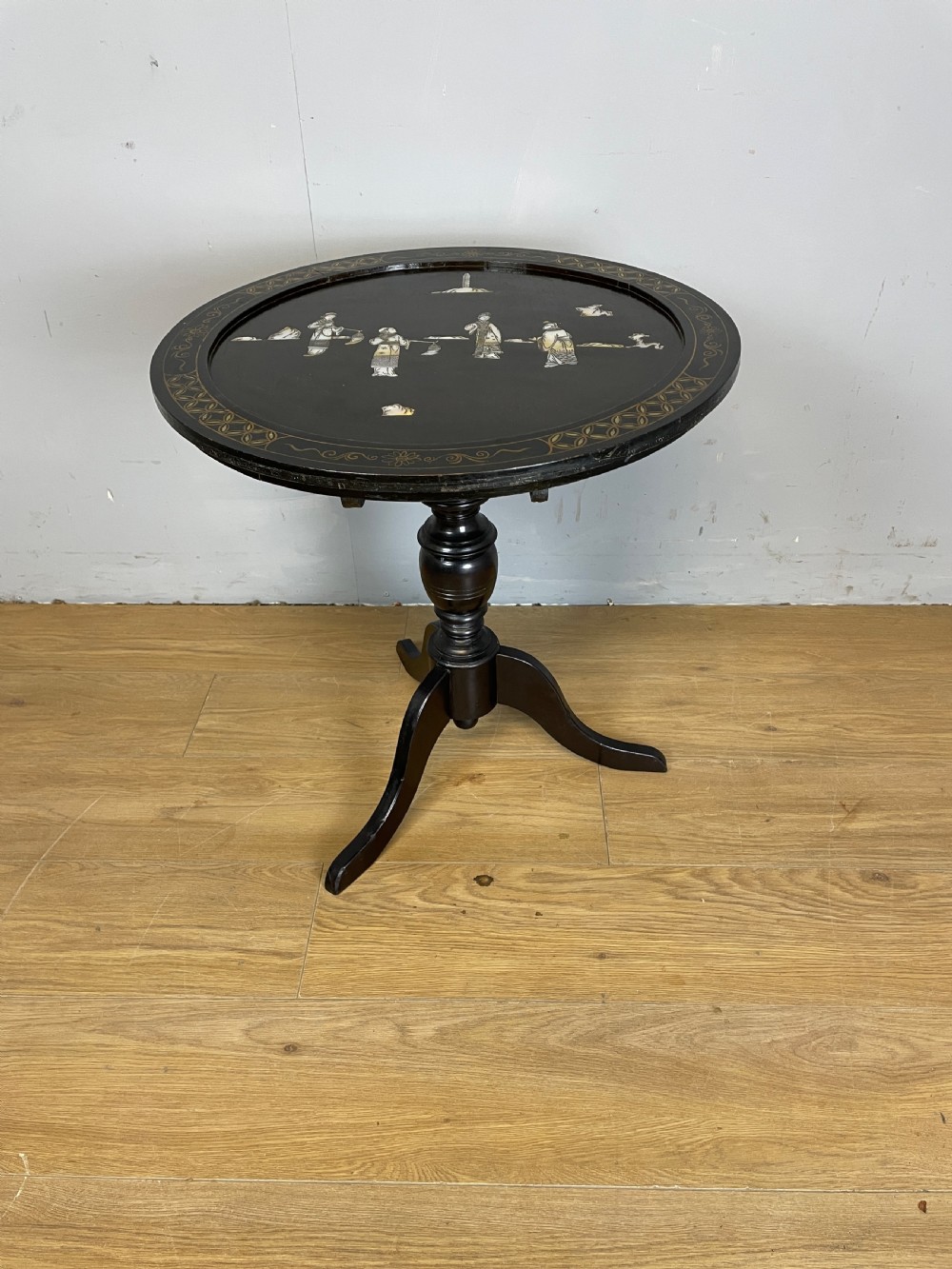 An Edwardian black lacquered circular tripod table decorated with mother-of-pearl figurative inlays and gilt floral borders. View II