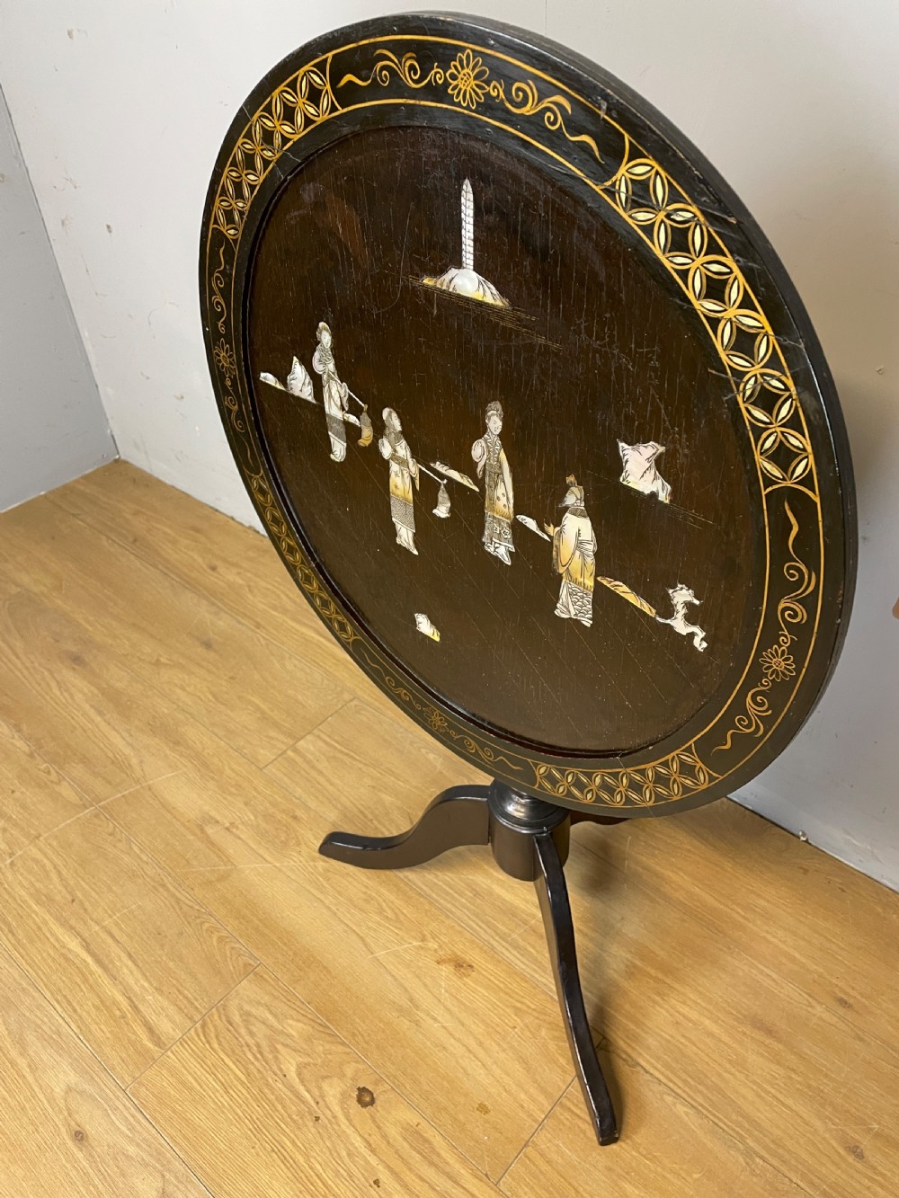 An Edwardian black lacquered circular tripod table decorated with mother-of-pearl figurative inlays and gilt floral borders. View V
