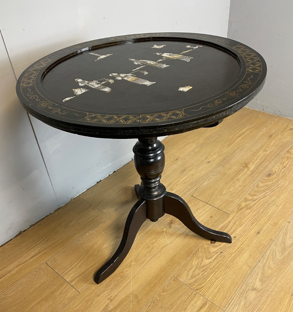 An Edwardian black lacquered circular tripod table decorated with mother-of-pearl figurative inlays and gilt floral borders. View X